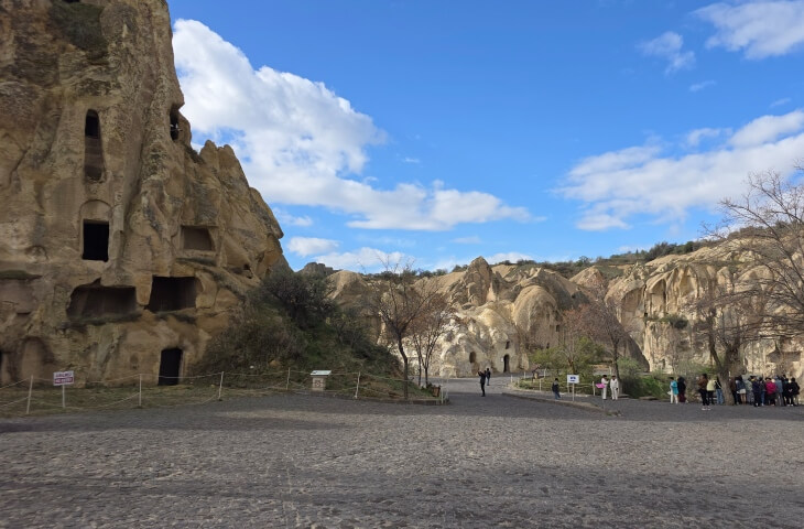 Göreme Açık Hava Müzesi'nde kaya içine oyulmuş yapılar ve alanda gezen ziyaretçiler açık havada görülüyor.